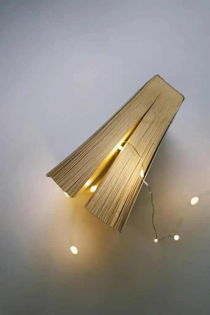 Open book with pages illuminated by string lights, creating a cozy indoor ambiance.